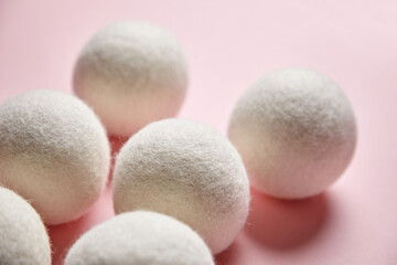 Soft white wool dryer balls arranged on a pastel pink background, showing natural wool texture. Eco-friendly laundry alternative emphasizing simplicity and sustainability