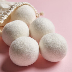 Wool dryer balls spilling out of a drawstring cotton bag on a pastel pink background. Ideal for sustainable, eco-friendly laundry solutions and minimalist design