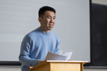 A man in a blue sweater is standing at a podium giving a speech