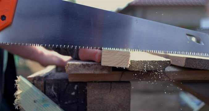Hand sawing plank with orange handle saw, super slow motion at 800 fps, close-up of precise woodwork, sawdust flying, manual labor in carpentry setting