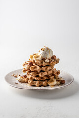 Homemade waffles stack with ice cream, bananas and nuts on white plate isolated on white background, text space