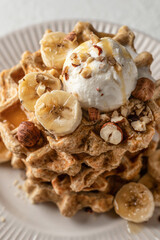 Homemade waffles stack with ice cream, bananas and nuts on white plate close up