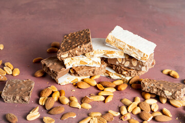 A close-up view of assorted nougat bars, featuring layers of chocolate, almonds, and peanuts arranged on a slate, showcasing texture and variety