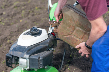 A man pours gasoline from the canister into the cultivator tank