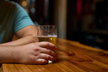 Close-up of a hand with a glass of beer on the bar