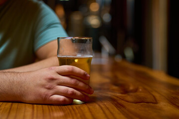 Close-up of a hand with a glass of beer on the bar