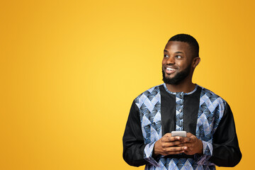 Happy black guy with modern smartphone looking at empty space, wearing african t-shirt, pink studio...