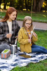 Naklejka premium Woman volunteer teaching little girl explaining how wind turbines produce renewable energy