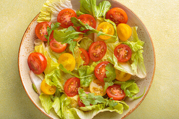 Fresh and vibrant mixed salad with crisp lettuce, juicy red and yellow cherry tomatoes and arugula. Served in a bowl with cutlery on the side. Vitamins and healthy eating habits