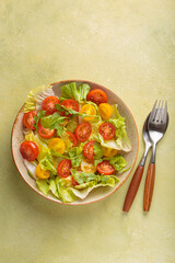Fresh and vibrant mixed salad with crisp lettuce, juicy red and yellow cherry tomatoes and arugula. Served in a bowl with cutlery on the side. Vitamins and healthy eating habits