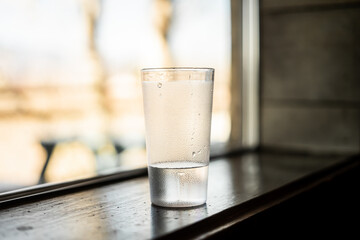Cold glass of water with condensation on a windowsill, natural light in the background