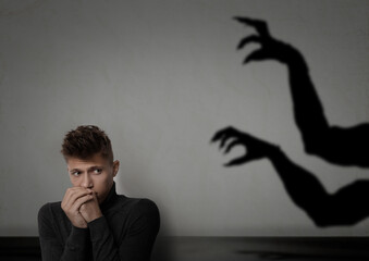 Young man scared by hands of monster reaching for him. Creepy shadow on grey wall © New Africa