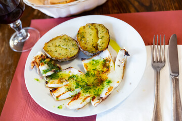 Close up fried potato halves with fried cuttlefish topped with spicy white garlic sauce on white plate