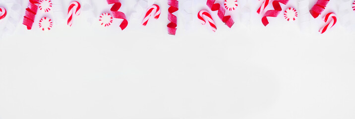 Christmas top border of red and white ribbon and peppermint candy canes. Overhead view on a white banner background with copy space.