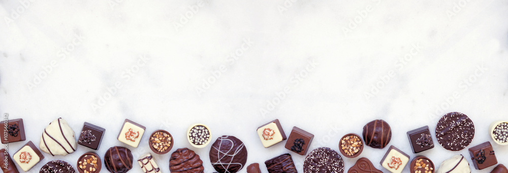 Poster chocolate bottom border with an assortment of fine, luxurious sweets. top view on a white marble ban