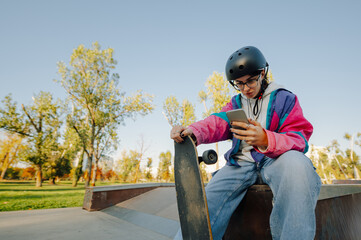 Young skater using phone and holding skateboard at skatepark