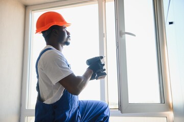 Young African Repairman In Overalls Installing Window