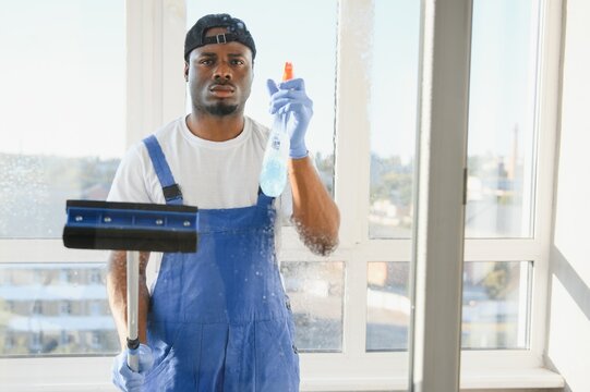 Male Worker Cleaning Glass With Squeegee And Spray Bottle - Powered by Adobe