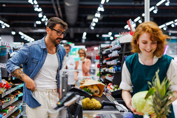 Fototapeta premium Customer watching cashier scanning groceries at supermarket checkout