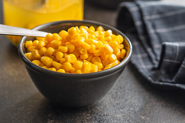 Canned sweet corn in bowl on black kitchen table.
