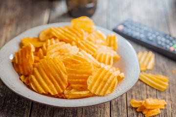 Crispy potato chips on plate on wooden table.