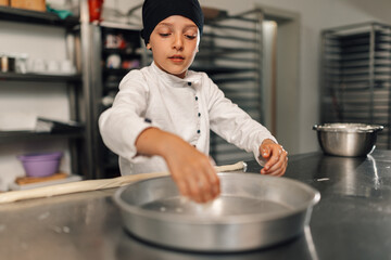 Focused young girl child chef sprinkling ingredients inside round baking pan.