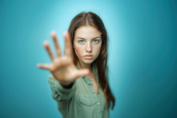 Fototapeta premium Young woman extends her hand forward, representing a stance against abuse and advocating for protective rights and laws. Her gaze is intense, conveying resilience and a call for justice. Blue backgrou