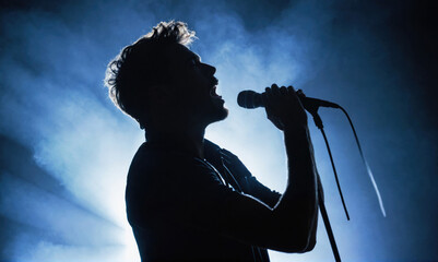 A silhouette of a singer performing on stage, bathed in blue light