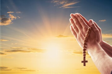 Human hands praying with Christian cross at sunrise