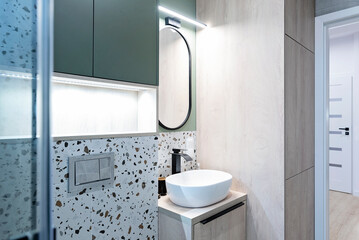 Interior of modern bathroom with ceramic bathroom sink with tap and textured tile on the wall. New apartment with circle mirror and LED light.