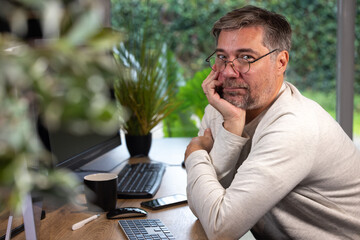 portrait d'un employé de bureau ou d'un homme d'affaires qui est assis à son bureau devant son ordinateur il est souriant et sympathique. Il est heureux de travailler chez lui à distance