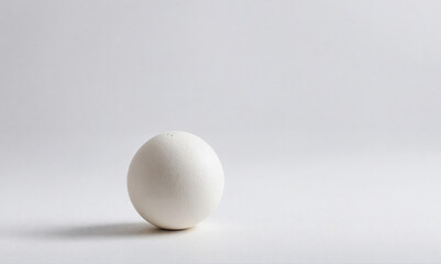 A single white egg sits on a white surface