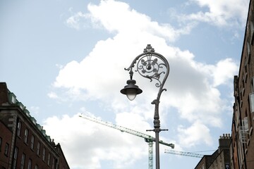 Elegant vintage street lamp against a blue sky with clouds, construction cranes on the background