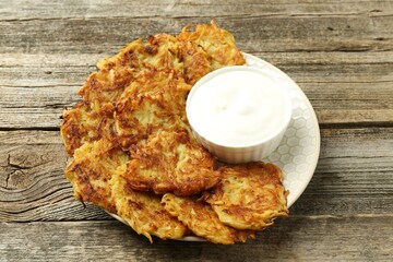 Delicious potato pancakes and sour cream on wooden table, closeup