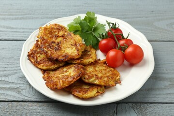 Delicious potato pancakes, tomatoes and parsley on gray wooden table, closeup