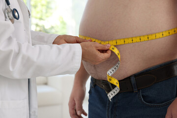 Nutritionist measuring overweight man's waist with tape in clinic, closeup