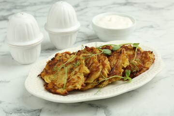 Delicious potato pancakes with fresh microgreens and sour cream on white marble table, closeup
