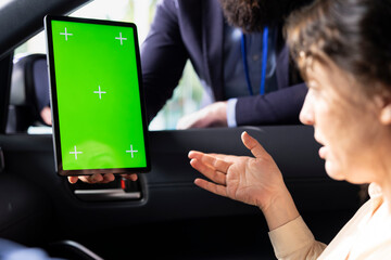 Car dealership worker holding chroma key device, asking driver questions to determine vehicle desired. Employee ensures clients satisfaction, showing cars on isolated screen tablet during test drive