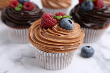 Tasty cupcakes with chocolate cream and berries on white marble table, closeup