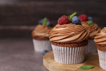 Tasty cupcakes with chocolate cream and berries on brown table, closeup. Space for text