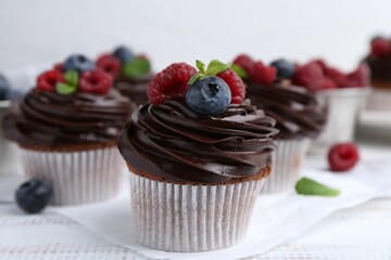 Tasty cupcakes with chocolate cream and berries on white wooden table, closeup