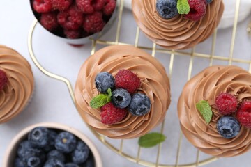 Tasty cupcakes with chocolate cream and berries on white table, flat lay