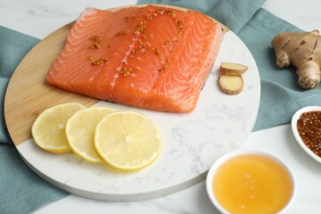 Salmon fillet with mustard, lemon slices, honey and ginger on white table, closeup