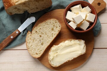 Fresh bread with butter and knife on light wooden table, flat lay