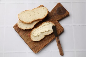 Fresh bread with butter and knife on white tiled table, top view