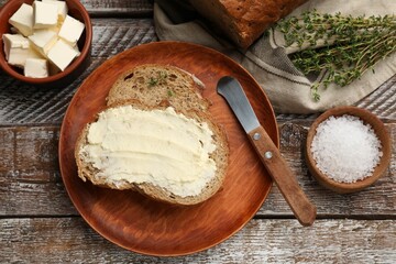 Fresh bread with butter, thyme, salt and knife on wooden table, flat lay