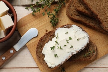 Fresh bread with butter, thyme and knife on light wooden table, flat lay