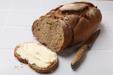 Fresh bread with butter and knife on white tiled table, closeup