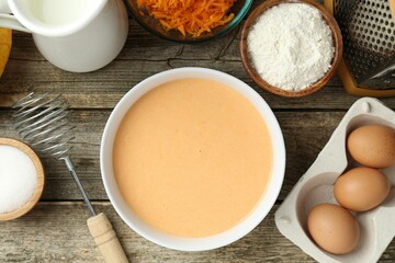 Bowl with dough and ingredients for pumpkin pancakes on wooden table, flat lay