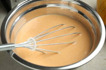 Bowl with dough for pumpkin pancakes and whisk on table, closeup